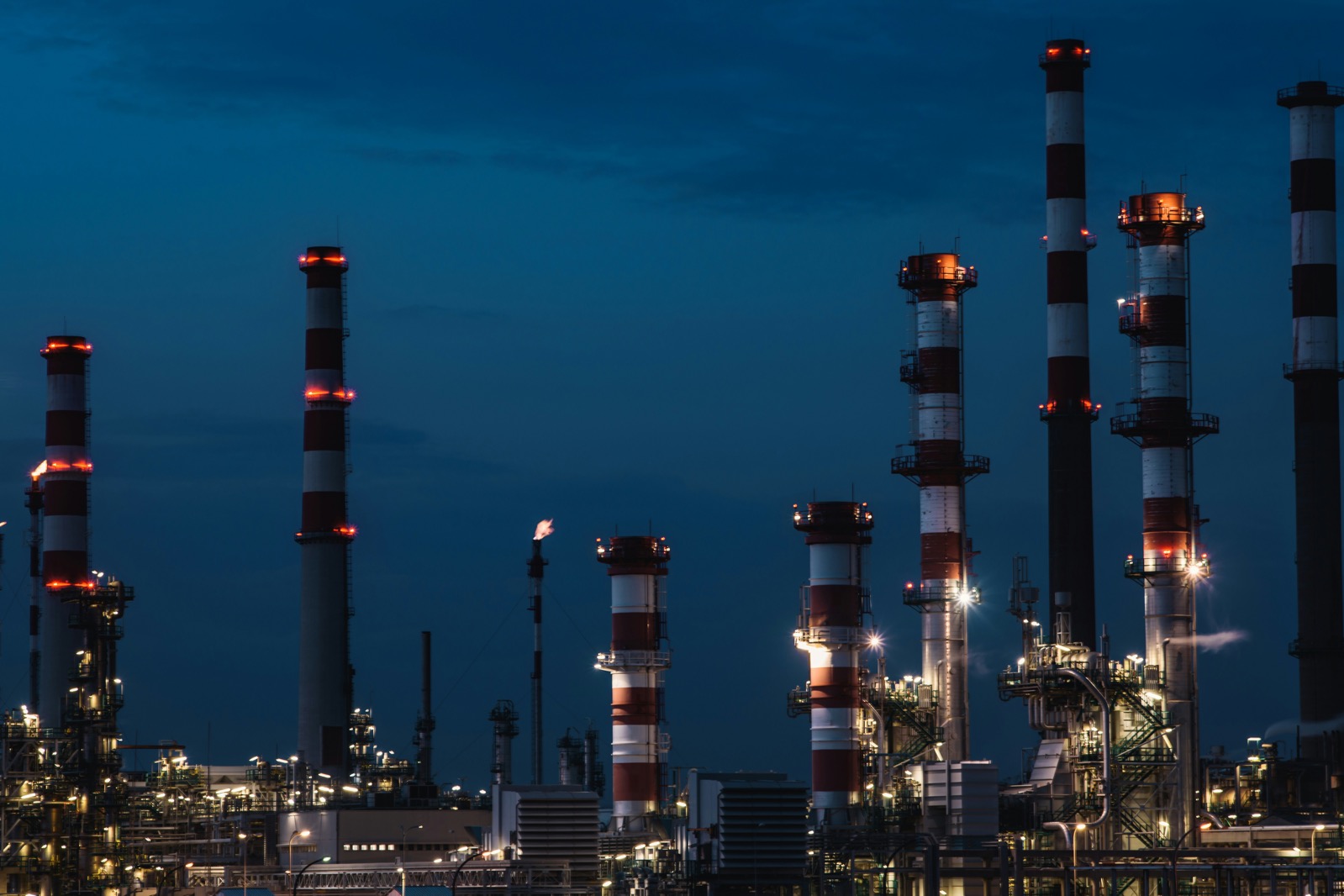 Beleuchtete Schornsteine und Rohrleitungen einer Chemieanlage bei Nacht