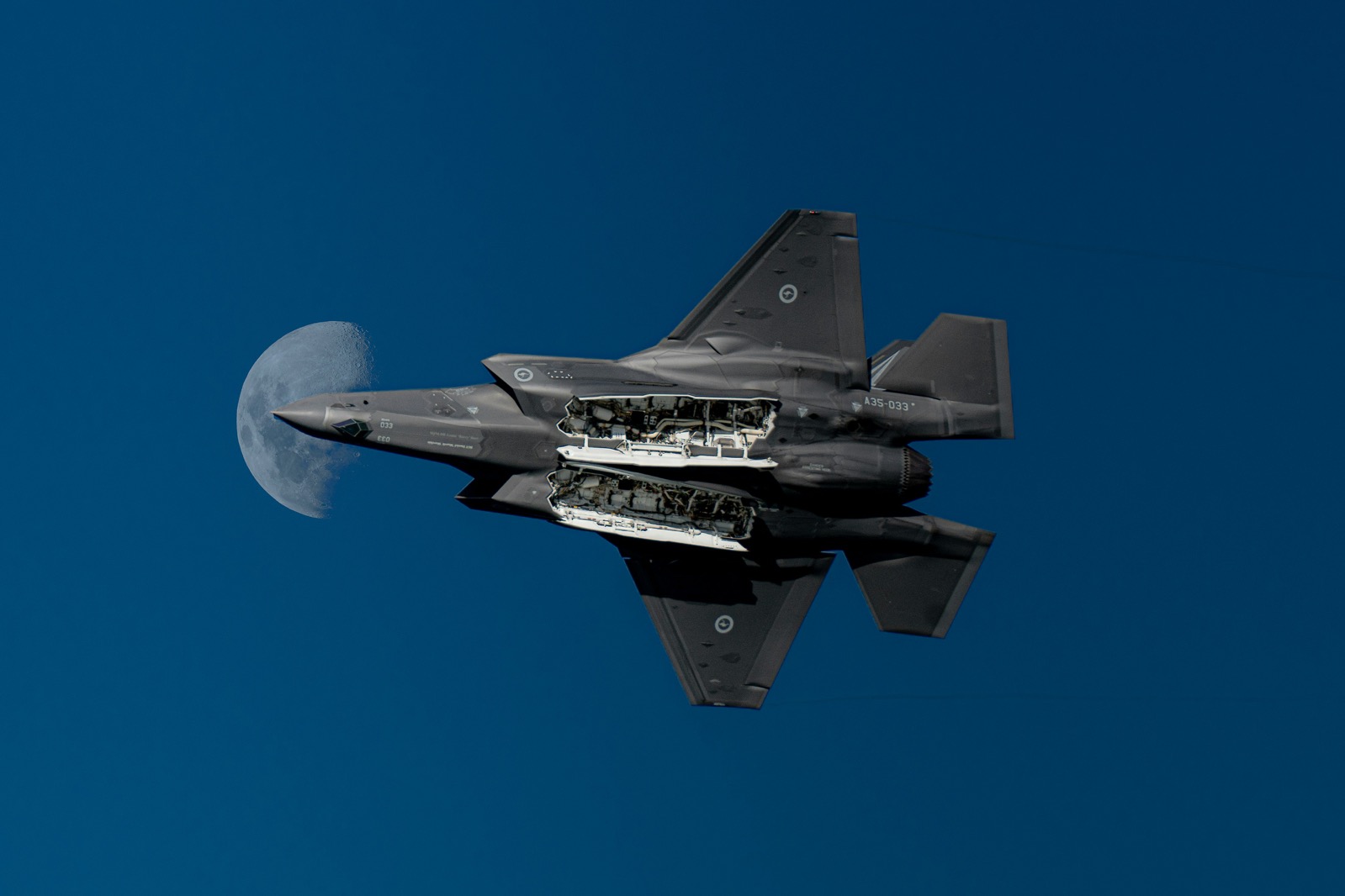 Kampfflugzeug im Flug vor dem Mond, geöffnete Wartungsklappe sichtbar